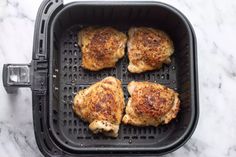 four pieces of chicken in a air fryer on a marble counter top, ready to be cooked