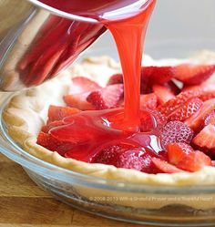 someone pouring syrup onto a pie with strawberries in it