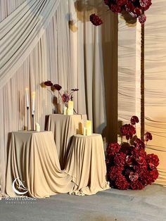 two tables with candles and flowers in front of a drapeed wall at a wedding reception