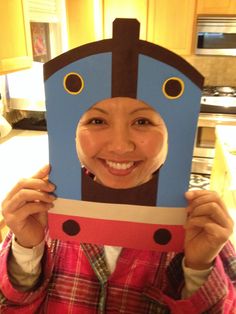 a woman holding up a cardboard train in front of her face and smiling at the camera