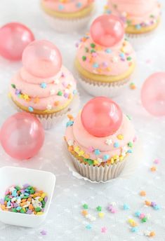 cupcakes with pink frosting and sprinkles on a white table