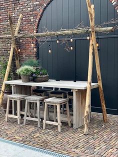 an outdoor dining table with stools and potted plants next to it on a brick patio