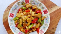 a plate filled with chicken and peppers on top of a wooden cutting board next to chopsticks