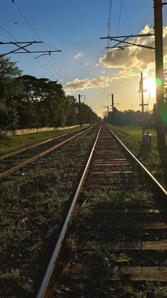 the sun shines brightly through power lines on an empty train track in this rural area