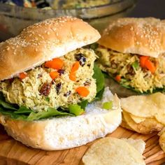 two chicken salad sandwiches with lettuce and carrots on a wooden cutting board