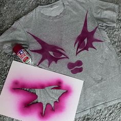 a t - shirt with purple paint on it next to a spray can and an acrylic