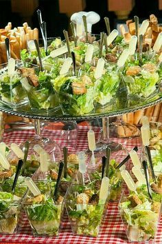 a table topped with lots of salads and french fries on top of a red checkered table cloth