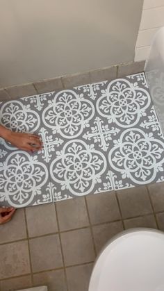 a person standing on a bathroom floor next to a bathtub and rug with an intricate design