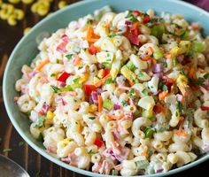 a blue bowl filled with macaroni salad on top of a wooden table next to vegetables