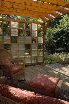 a covered patio area with wicker furniture and red cushions on the floor, surrounded by greenery