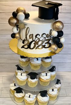 a graduation cake and cupcakes are arranged on a tiered tray with the words class of 2013 written on it