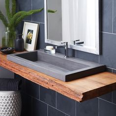 a bathroom sink sitting under a mirror on top of a wooden counter next to a potted plant