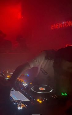 a dj mixing music at a party in the dark with red and green lights behind him