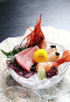 a bowl filled with different types of food on top of a stone slab next to a body of water