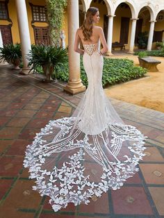 a woman standing in front of a building wearing a wedding dress with flowers on it