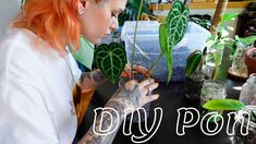 a woman with red hair is looking at some plants in a glass vase on a table