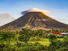 a large mountain with a red roof and trees around it in the foreground, surrounded by greenery