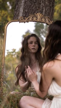 a woman sitting on the ground in front of a mirror looking at her hair and makeup