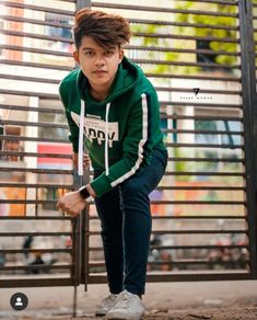 a boy in a green hoodie leaning against a fence with his hand on the ground