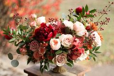 a vase filled with lots of flowers on top of a wooden table next to trees