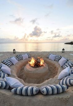 a fire pit on the beach with pillows around it