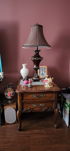 a table with a lamp and other items on it in a room that has pink walls