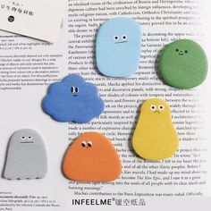 four different colors of buttons with eyes and mouths on top of an open page in a book