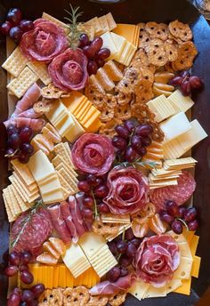 an assortment of cheeses, crackers and meats on a platter with grapes