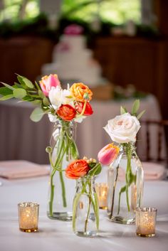 three vases filled with flowers sitting on top of a white tablecloth covered table