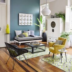 a living room with blue walls and yellow chairs on the floor, green plants in vases