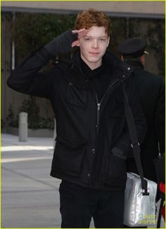 the young man is wearing a black jacket and holding his hand up to his head