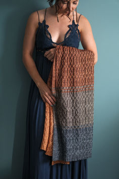 a woman in a blue dress is holding an orange and gray blanket over her shoulder