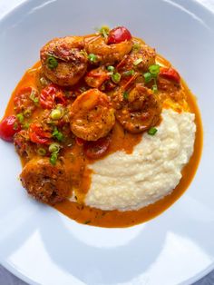 a white plate topped with mashed potatoes covered in shrimp and tomato gravy