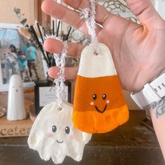 a hand holding two small halloween decorations in it's palm, one is orange and the other is white