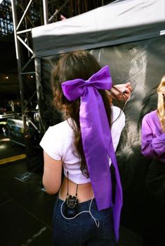 a woman with a purple bow on her head and earphones around her neck, standing in front of a stage