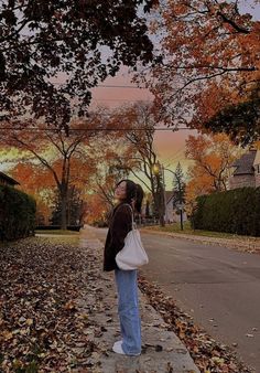 a woman standing on the side of a road with her hand in her pocket and looking up into the sky