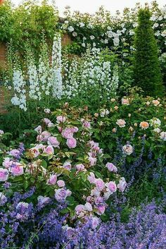 a garden filled with lots of flowers next to a brick wall covered in greenery