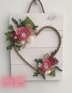 a heart shaped sign with flowers and leaves on it's side hanging from a rope