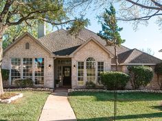 a brick house with green grass and trees in the front yard on a sunny day