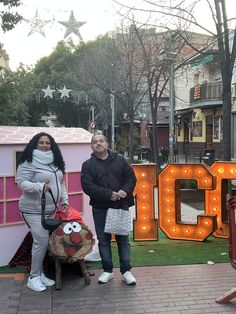 two people standing in front of a neon sign that says'coco'and a chicken bag