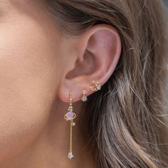 a woman wearing gold earrings with white and pink stones on the side of her ear