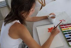 a woman sitting at a table painting with watercolors