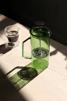 a green pitcher sitting on top of a wooden table next to a glass filled with water