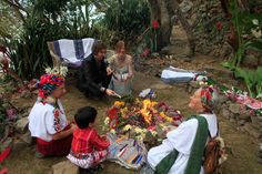 several people sitting around a fire pit with flowers and blankets on the ground in front of them