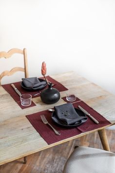 a wooden table topped with black plates and silverware next to a red place mat