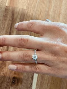 a woman's hand with a diamond ring on top of her left hand and a wooden table in the background