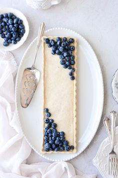 a white plate topped with a piece of pie covered in blueberries next to two spoons