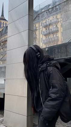 a woman with long black hair leaning against a building