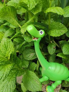 a green toy dinosaur standing in the middle of leaves and plants with its mouth open