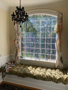 a window seat in front of a chandelier with curtains hanging from it's sides